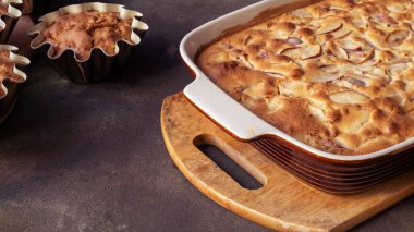 Turta ya da elmalı kek ve mutfakta çay olan bej ahşap tahta tahta. Koyu arkaplanda bir tabakta kırsal elmalar. konsept-sonbahar hasat yemekleri