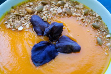Mavi arka planda mor fesleğenli balkabağı çorbası ve kızarmış kabak çekirdeği. Manzara, yemek fotoğrafları, yemek tarifleri, dergiler