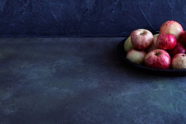 Vitaminlerle dolu kırmızı taze elma yığını yuvarlak metalik plaka ve mutfaktaki eski çizik beton masa üzerinde yatıyor. Hasat ya da diyet, otomatik konsept. Metin için boşluk