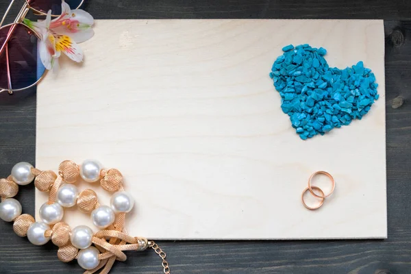 Mock up Valentine's day composition. a heart spilled out of small blue stones on a wooden Board with women's beads, glasses and rings. Top view, flat lay, copy space.