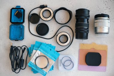 Video ışığı, lens filtreleri, polarizör, gradyan ve adaptör halkaları, ve gri arka grond üzerinde flash diskleri olan bir kutu. Profesyonel fotoğrafçı için ekipmanla düz kompozisyon