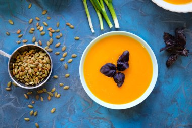 Mavi arka planda mor fesleğenli balkabağı çorbası. Üst Manzara, ayçekirdeği ve yeşil soğan, mavi arka planda servis kasesinde mor fesleğen..