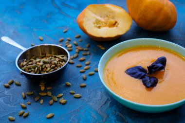 Mavi arka planda mor fesleğenli balkabağı çorbası. Üst Manzara, ayçekirdeği ve yulaf ezmesi, mavi arka planda servis kasesinde mor fesleğen. Üst Görünüm