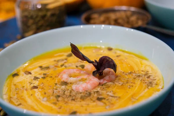Autumn food - pumpkin soup with cream, shrimps and seeds in bowls on table. pumpkin soup decorated with pumpkin seeds and toasted crackers on a dark blue background. Served for dinner View from above — Stock Image Autumn Food Pumpkin Soup Cream Shrimps Seeds Bowls Table Pumpkin Stock Image
