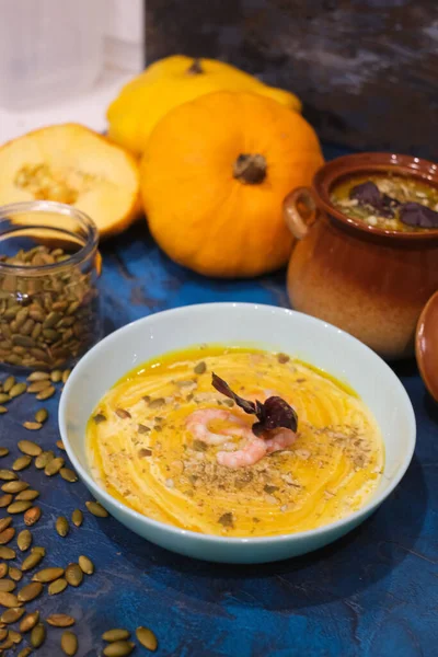 Autumn food - pumpkin soup with cream, shrimps and seeds in bowls on table. pumpkin soup decorated with pumpkin seeds and toasted crackers on a dark blue background. Served for dinner View from above — Stock Image Autumn Food Pumpkin Soup Cream Shrimps Seeds Bowls Table Pumpkin Stock Photo