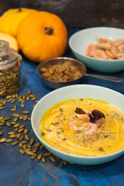Autumn food - pumpkin soup with cream, shrimps and seeds in bowls on table. pumpkin soup decorated with pumpkin seeds and toasted crackers on a dark blue background. Served for dinner View from above — Stock Image Autumn Food Pumpkin Soup Cream Shrimps Seeds Bowls Table Pumpkin Stock Picture