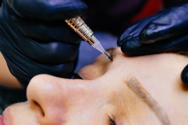 Usta kaş sanatçısı toz tarayıcı tekniğinde kalıcı kaş makyajı yapar. Kirpiğe kalıcı makyaj uygulanıyor. Usta, kaşlarla çalışır. Yarı kalıcı makyaj malzemesi.