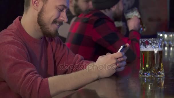 Хлопець друкує на своєму смартфоні в пабі — стокове відео