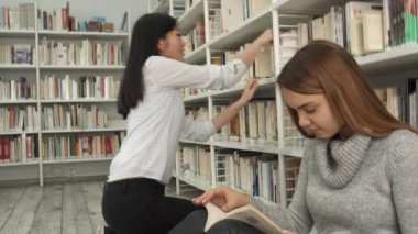 Kız kitap raf kütüphanede alır.