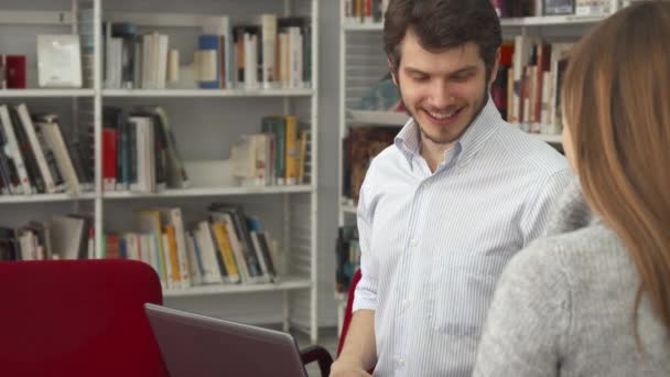 Чоловік студент показує свою однокласницю щось на ноутбуці в бібліотеці — стокове відео