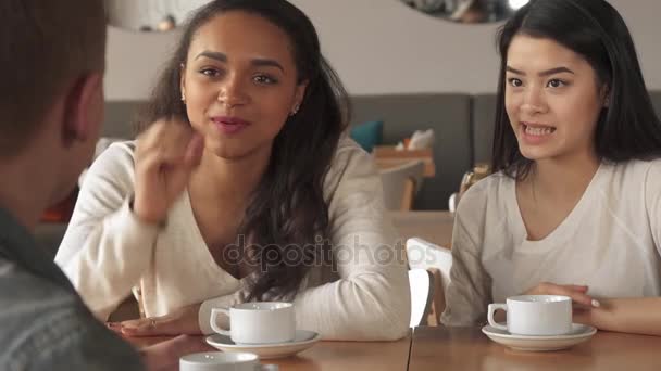 Две девушки рассказывают что-то своему другу-мужчине в кафе — стоковое видео