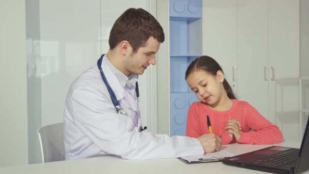 Pediatrician draws on clipboard near the little girl — Stock Video