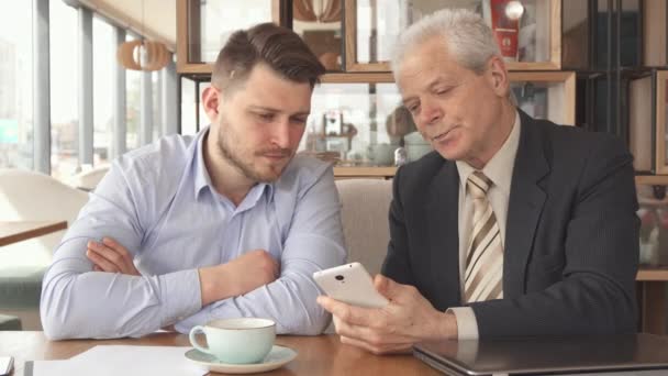 Старший бизнесмен показывает своему партнеру что-то на своем смартфоне — стоковое видео