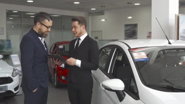 Менеджер по продажам разъясняет клиенту договор в автосалоне — стоковое видео
