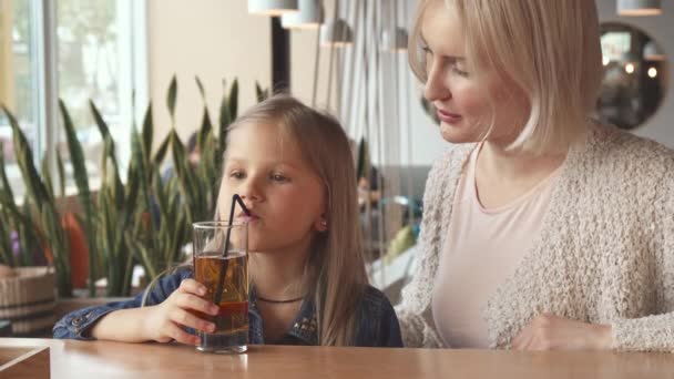 Menina bebe um pouco de bebida através de uma palha no café — Vídeo de Stock