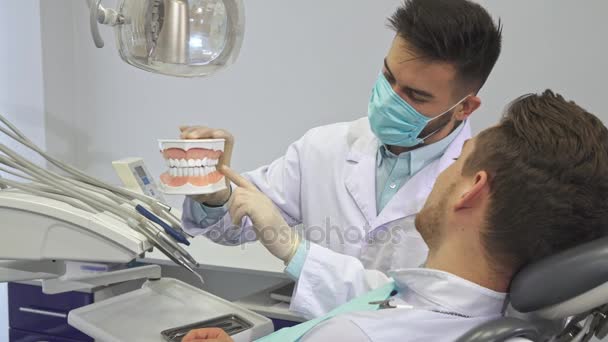 Dentysta pokazuje klienta układ zębów ludzkich — Wideo stockowe