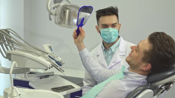 O paciente olha para os dentes no espelho no consultório do dentista. — Vídeo de Stock