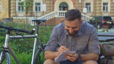Bisikletçi onun not defterinde bankta yazıyor.