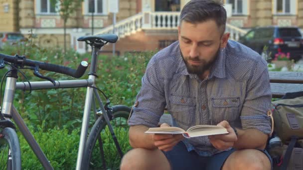 Cyklista čte knihu na lavičce — Stock video