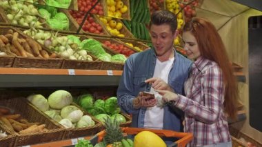 Çift smartphone süpermarkette alışveriş listesi tartışır