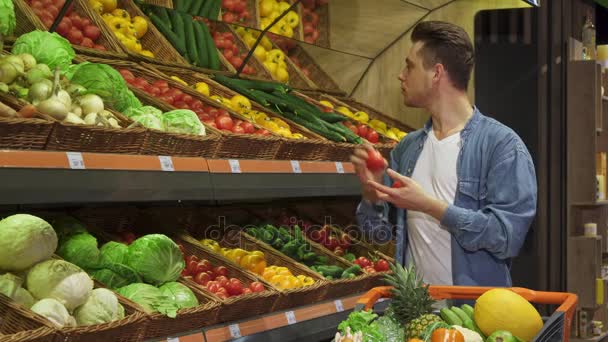 Мужчина берет помидоры и огурцы из стойки в супермаркете — стоковое видео