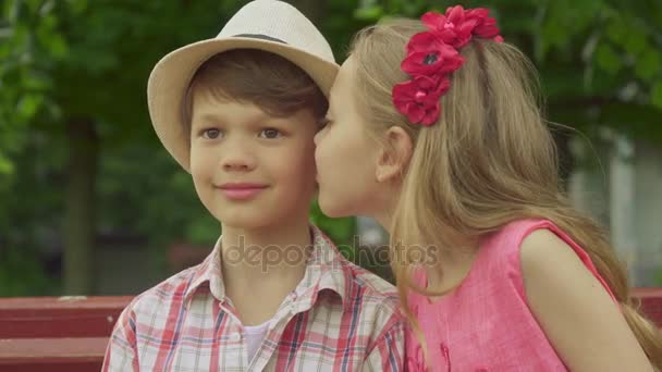 Little girl kisses boys cheek on the bench — Stock Video