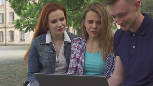 Los jóvenes ven algo en la computadora portátil en el campus — Vídeos de Stock