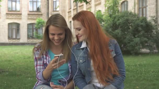 Estudantes do sexo feminino ouvem música no smartphone no campus — Vídeo de Stock