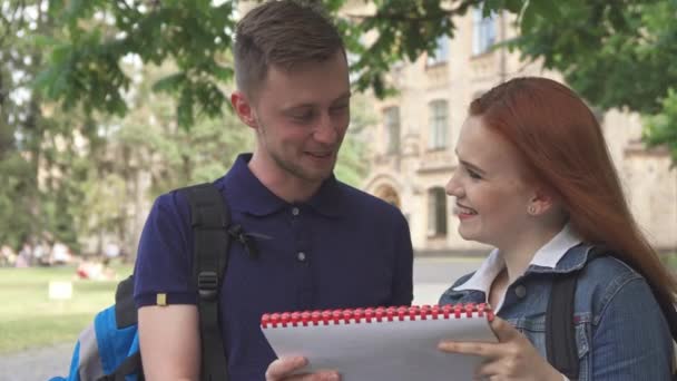 Estudante pergunta a seu colega sobre algo no caderno no campus — Vídeo de Stock