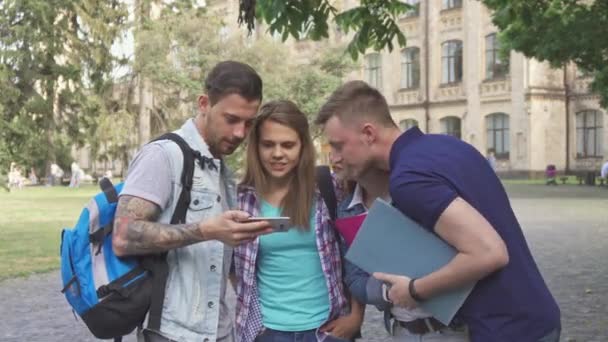 Cuatro estudiantes miran la pantalla del teléfono inteligente en el campus — Vídeos de Stock