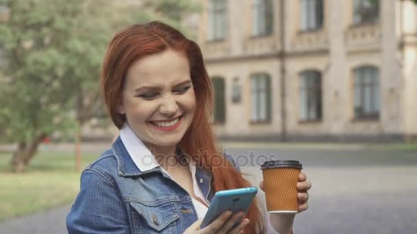 女子学生は笑う彼女がキャンパス内にスマート フォンで見る — ストック動画