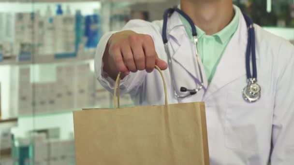 Médico sonriendo y sosteniendo un paquete en la farmacia — Vídeos de Stock