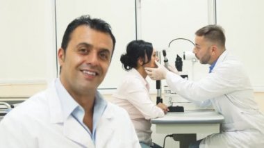 Arka plan üzerinde başka bir doktor hasta incelerken gülümseyen bir doktor oturur