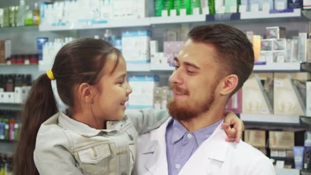 Um farmacêutico amigável está segurando uma menina em seus braços — Vídeo de Stock