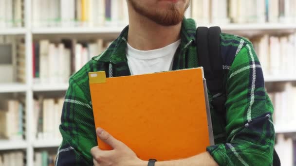 Ένας νεαρός φοιτητής με τα σχολικά βιβλία στα χέρια του στέκεται στη βιβλιοθήκη — Αρχείο Βίντεο
