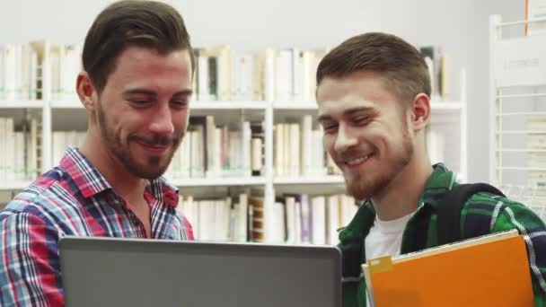 Två unga studenter skratta stående i biblioteket — Stockvideo