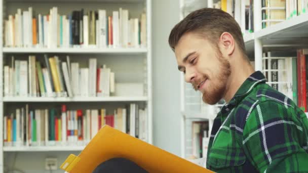Smějící se chlap sedí v knihovně a čtení — Stock video