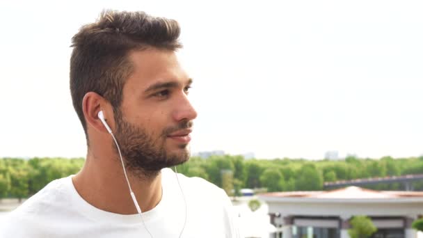 Um jovem ouve algo em seus fones de ouvido e ri — Vídeo de Stock