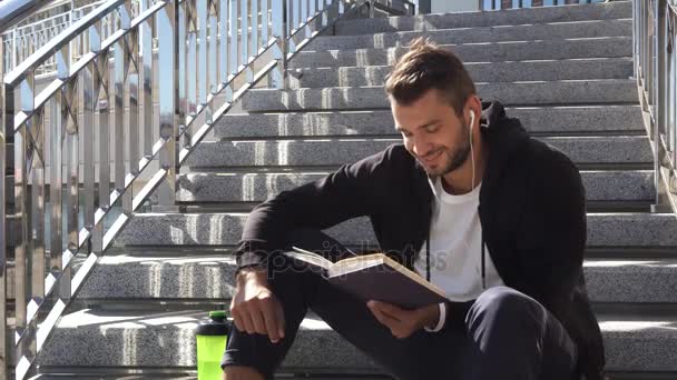 El tipo tranquilo está leyendo un libro sentado en las escaleras. — Vídeos de Stock