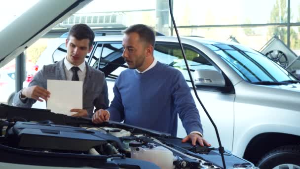 Egy figyelmes vevő és az eladó tanul a részleteket a nyitott motorháztető az autó — Stock videók