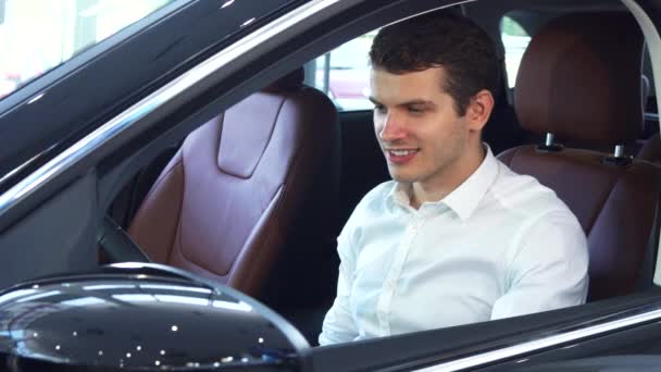 Ένας νεαρός άνδρας κρατά το τιμόνι ενός νέου αυτοκινήτου — Αρχείο Βίντεο