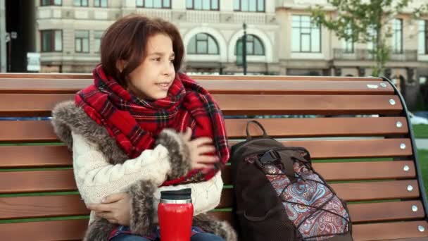 Krásná dívka je zima, sedí na lavičce — Stock video