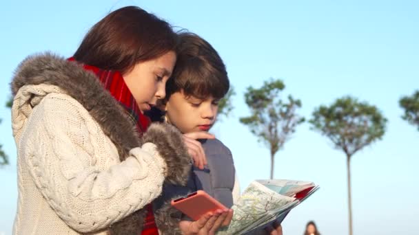 Les enfants actifs essaient de trouver le prochain endroit de leur itinéraire avec une carte et un téléphone mobile — Video