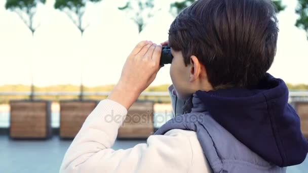 Een leuke jongen onderzoekt de buurt door middel van verrekijkers — Stockvideo