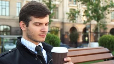 Genç bir adam bir bankta oturur ve kahve içer