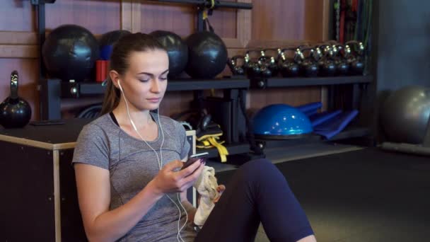 The girl is listening to music on headphones during a break between training sessions — Stock Video