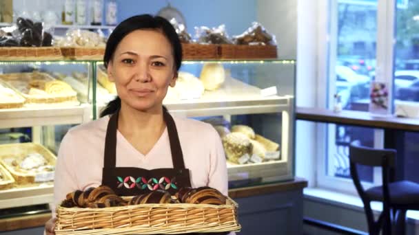 Madura hembra panadero posando en su tienda con una cesta llena de croissants — Vídeos de Stock