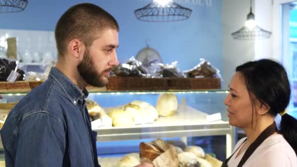 Pohledný mladý muž koupí čerstvý chléb od ženské baker — Stock video