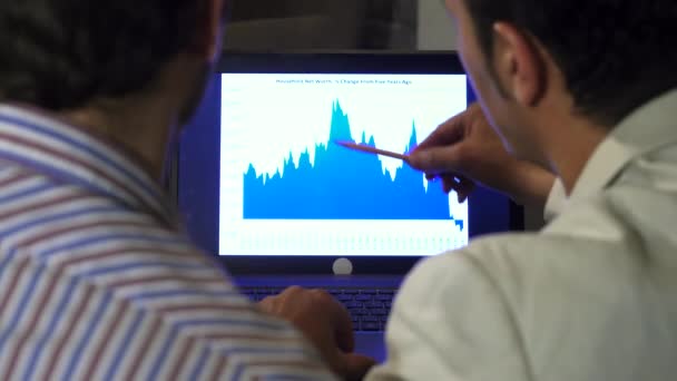 Задній перегляд крупним планом двох бізнесменів, які обговорюють діаграму на екрані ноутбука — стокове відео