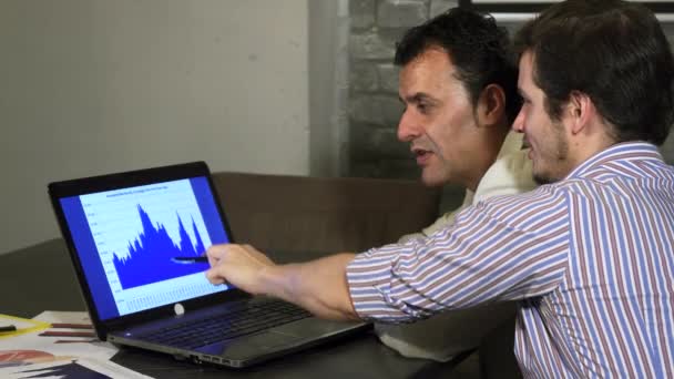 Два бизнес-коллеги обсуждают диаграмму на ноутбуке — стоковое видео